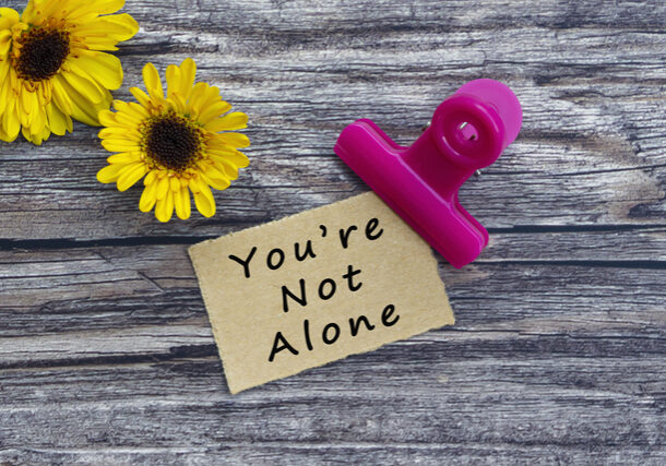 You are not alone text on torn brown paper with paper clip holder on wooden surface. Motivational quote.